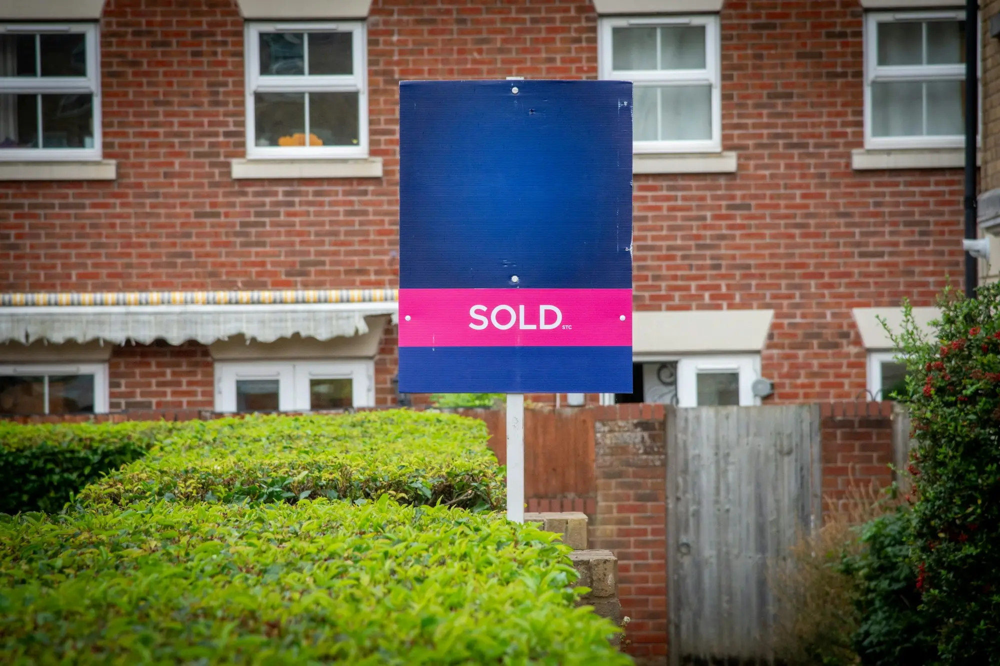 SOLD sign on a post in front of a red-brick townhouse behind a clipped hedge, the outcome an owner with an ATO judgment debt wants to avoid