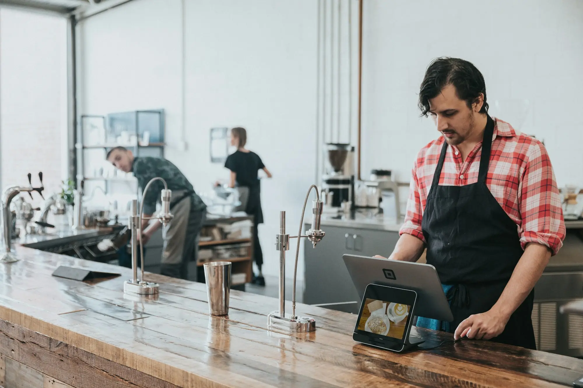 New cafe owner in an apron checking orders on a tablet at the wooden counter