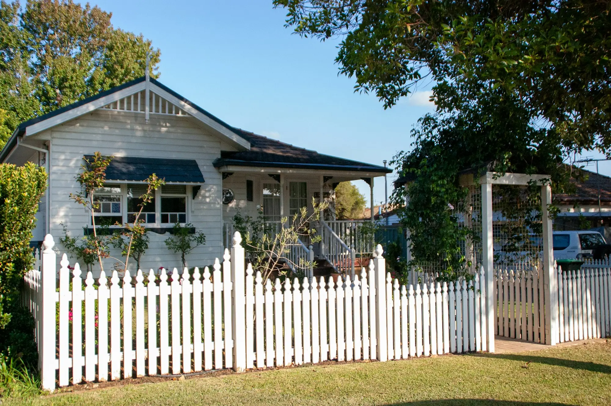 White weatherboard home behind a white picket fence and leafy garden in an Australian suburb