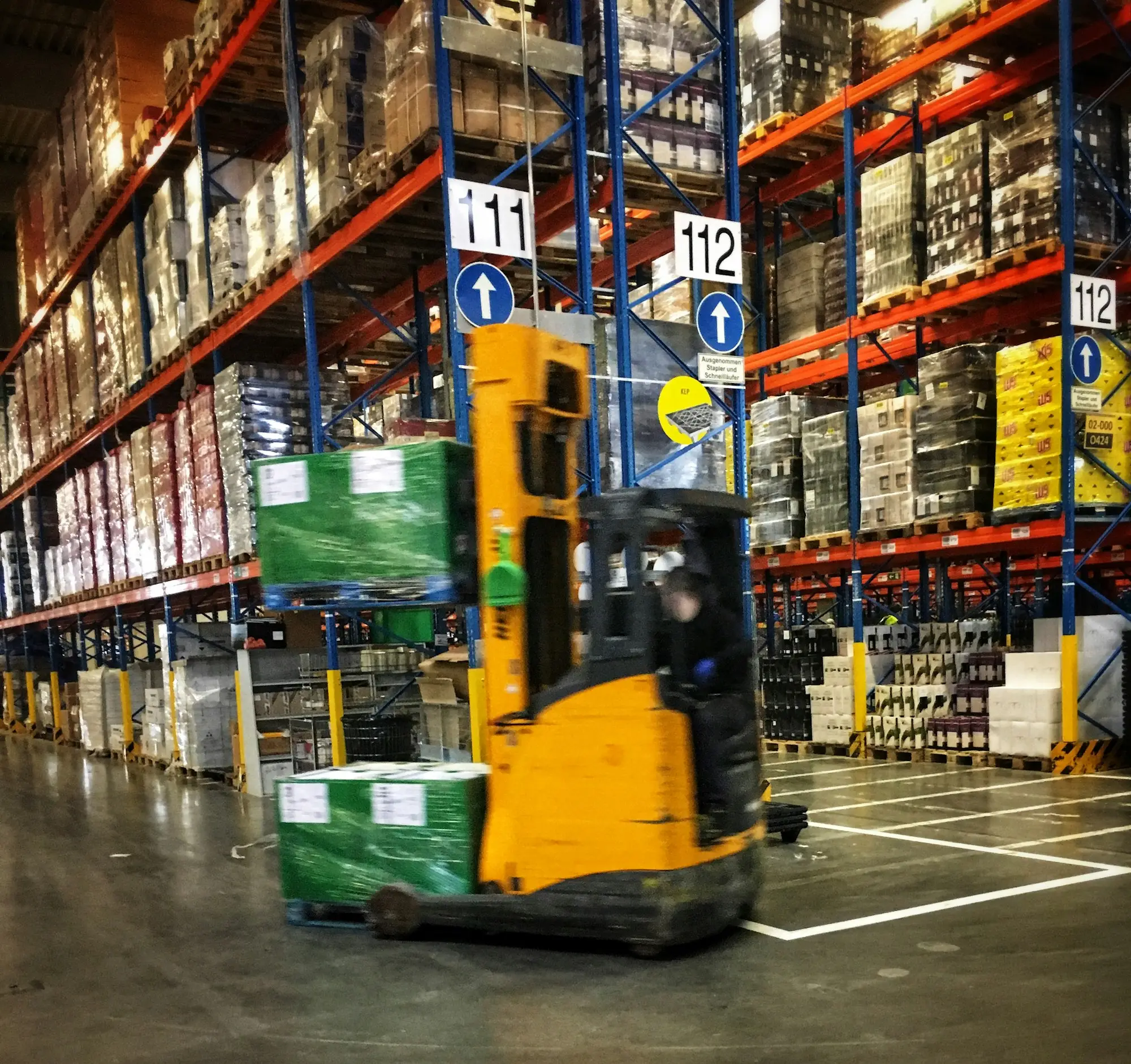 Forklift moving through a warehouse aisle stacked with pallets of stock before the end of financial year