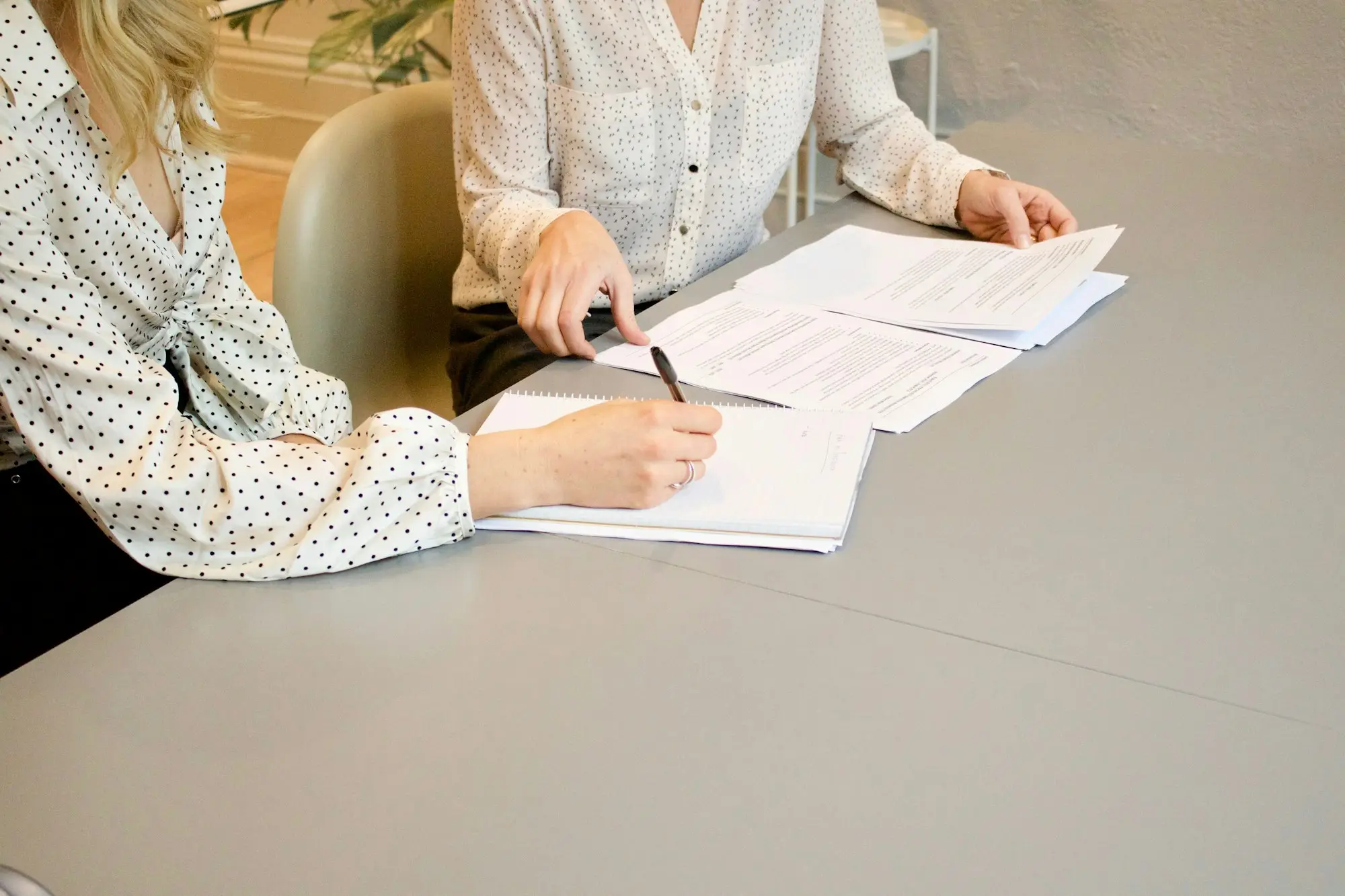 Business owner signing private loan documents while a lending specialist points out the next page