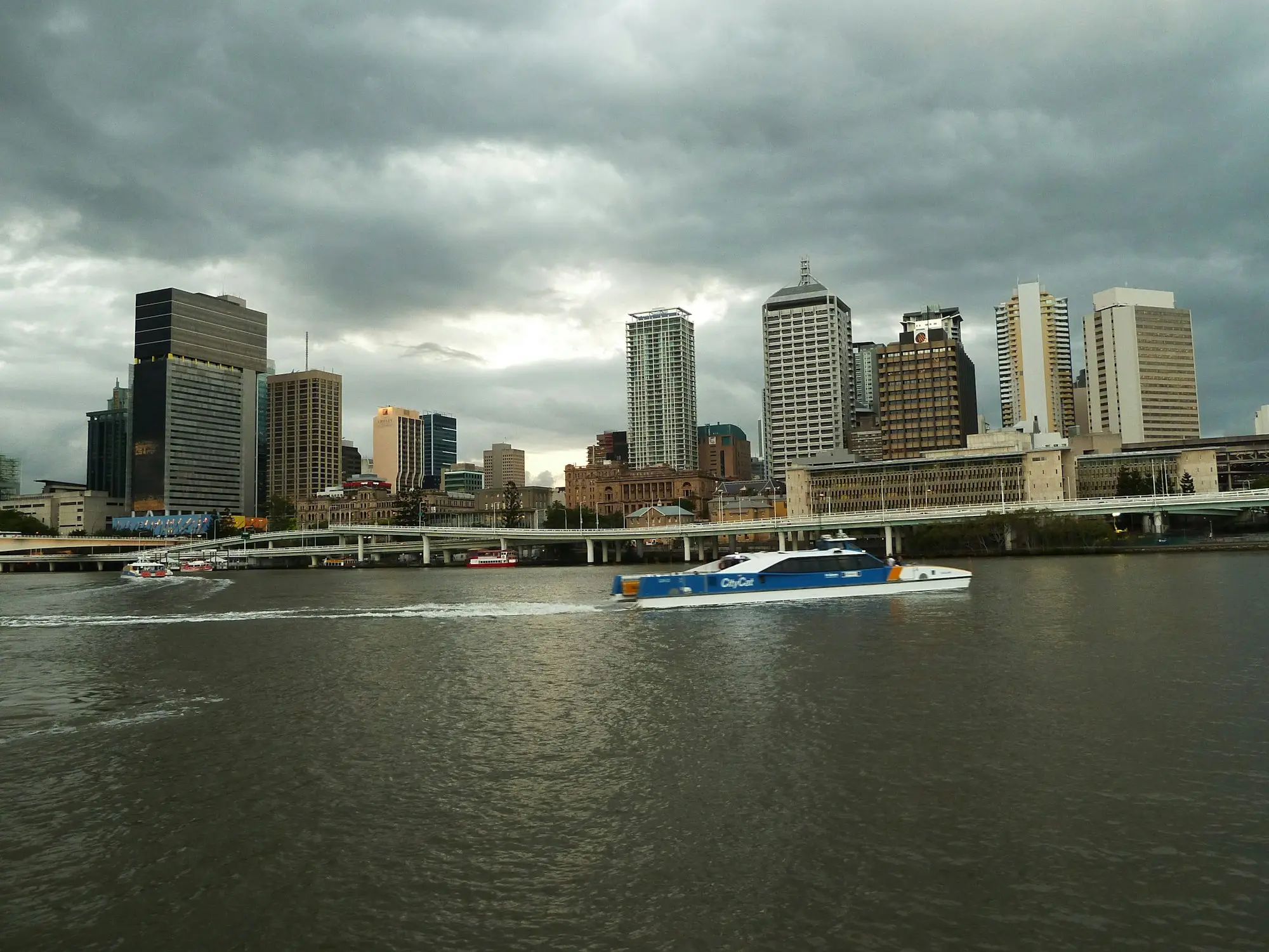 Brisbane skyline and river with a CityCat ferry under a stormy sky