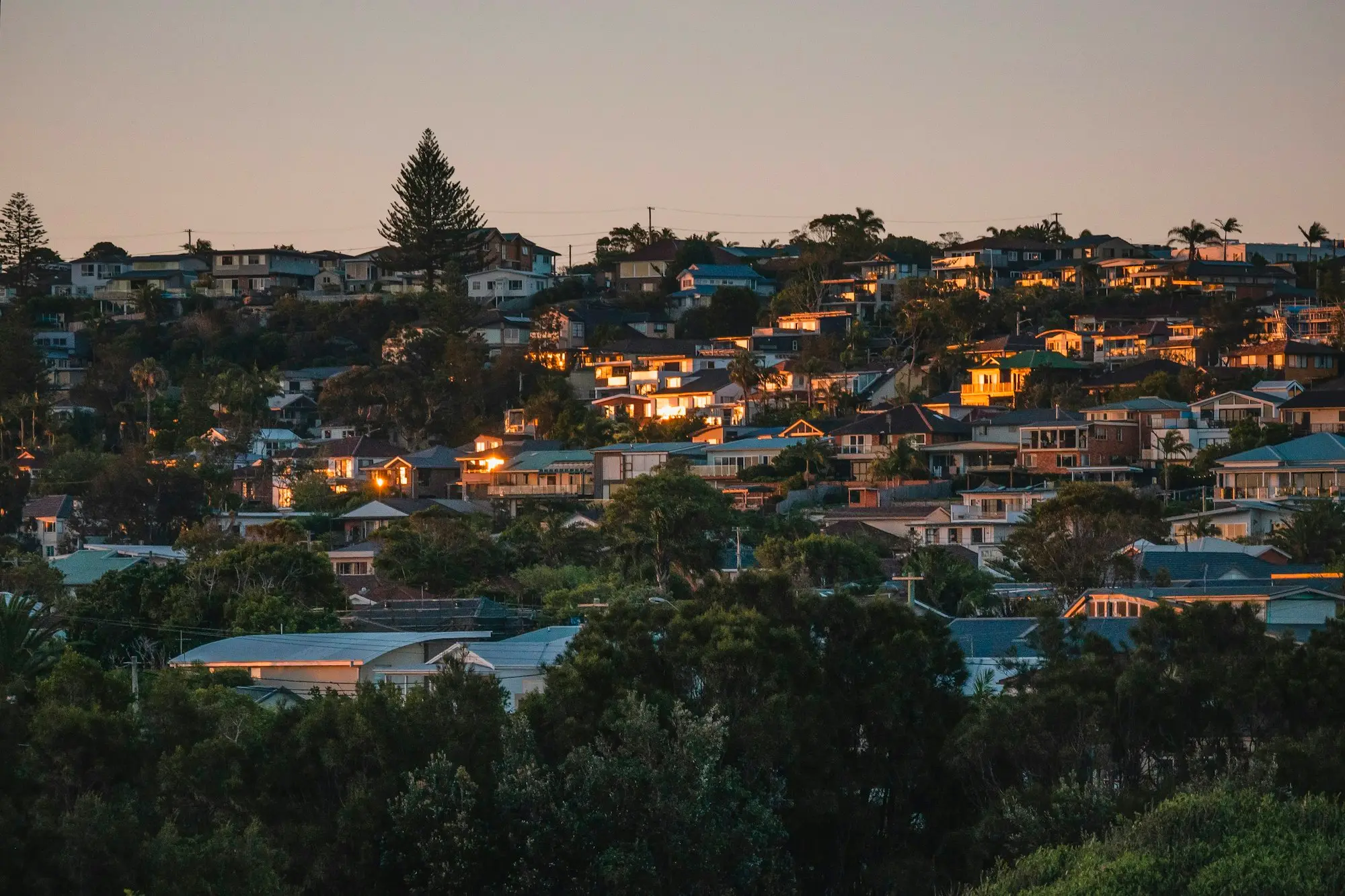 Suburban homes on a hillside lit up at dusk in an Australian city